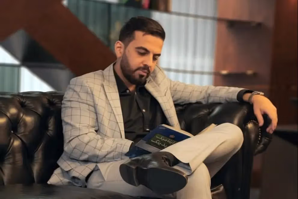 Cryptoland CEO Sina Estavi sitting on a couch, reading thoughtfully — The Coinomist.