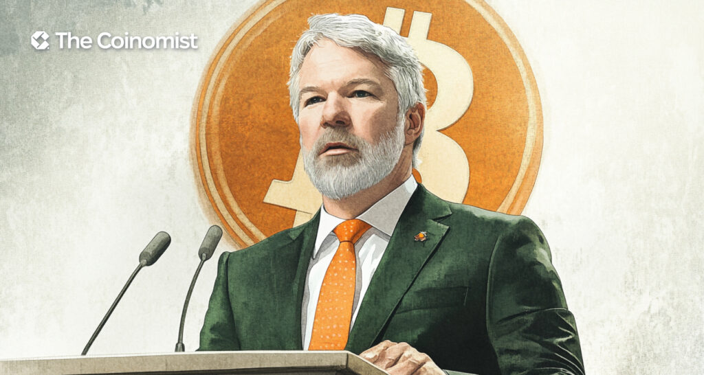 Michael Saylor wearing an orange tie, speaking at a podium with the X and Bitcoin logos in the background - The Coinomist