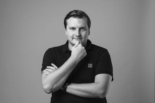 Stani Kulechov in a black polo shirt with arms crossed and hand on chin, posing for a black-and-white portrait — The Coinomist