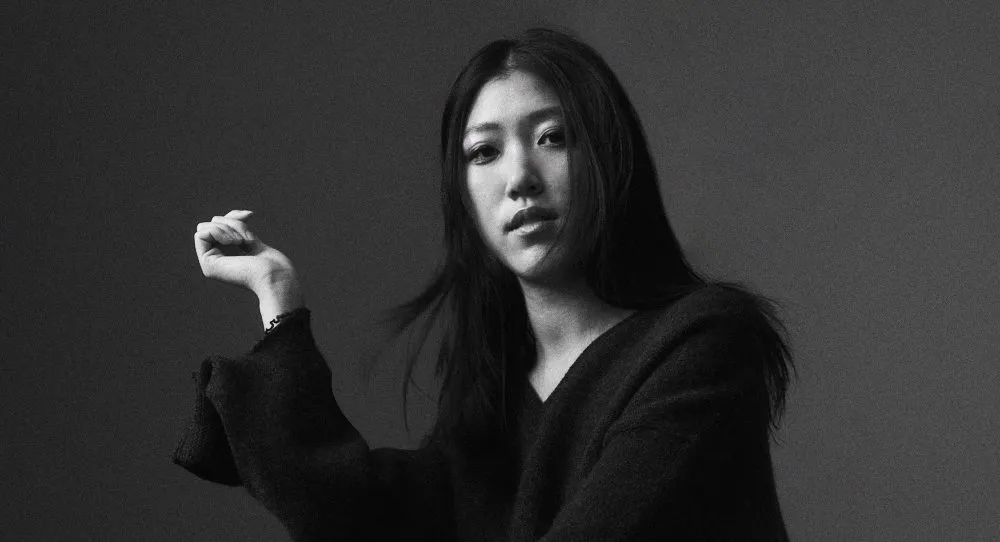 Emily Yang poses in sculptural black knitwear, captured in soft grayscale—embodying the quiet futurism and narrative depth she brings to both her style and her work. — The Coinomist