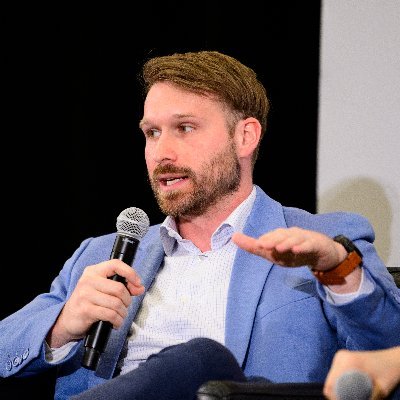 Photo of James Seyffart speaking at a panel, holding a microphone and gesturing during a discussion on crypto ETFs — The Coinomist.